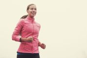 Junge Frau joggt durch Nebel und trägt pinke Jacke Junge Frau joggt durch Nebel und trägt pinke Jacke